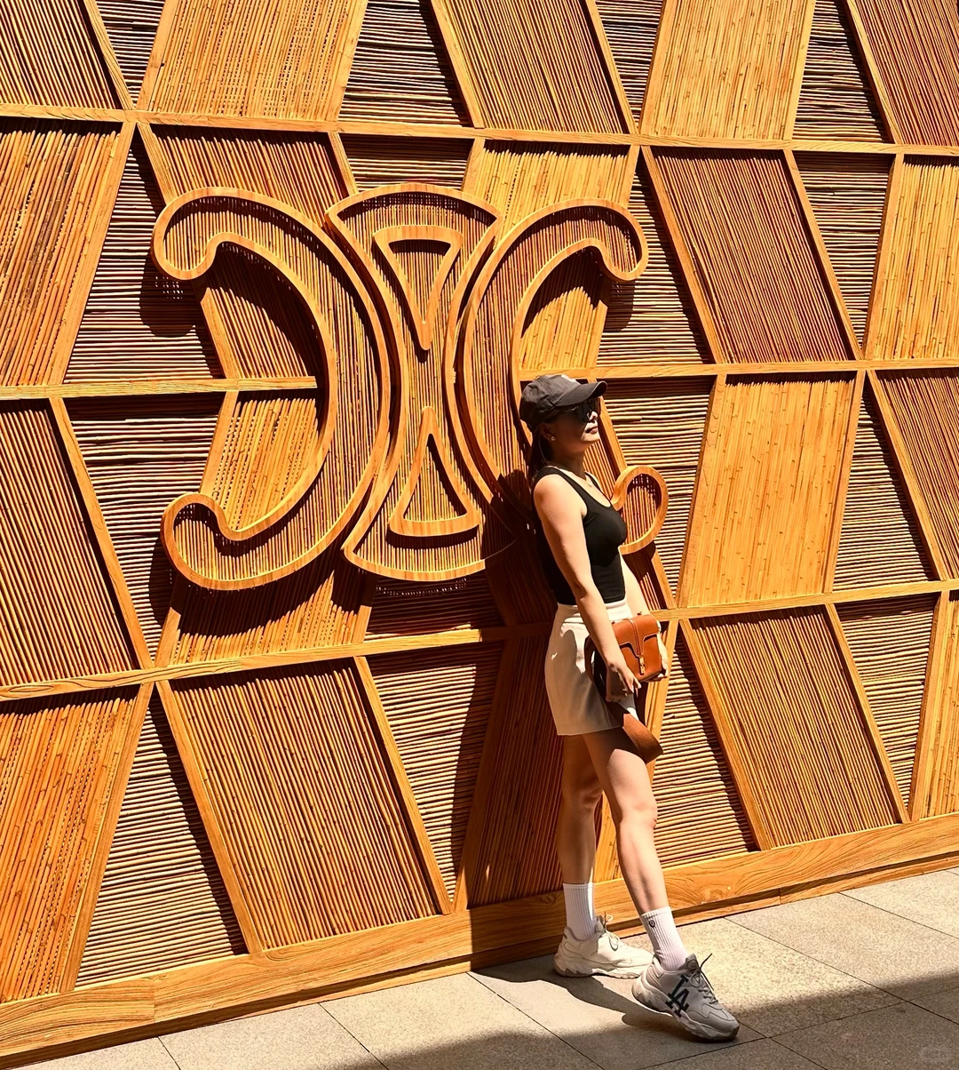 Alicia in a black top and white skirt against a sculptural timber wall