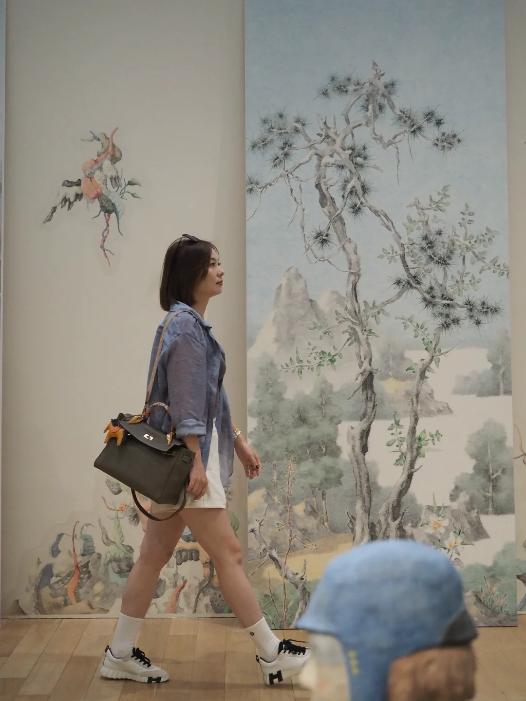 Alicia walking through an art gallery in a slate shirt and white shorts