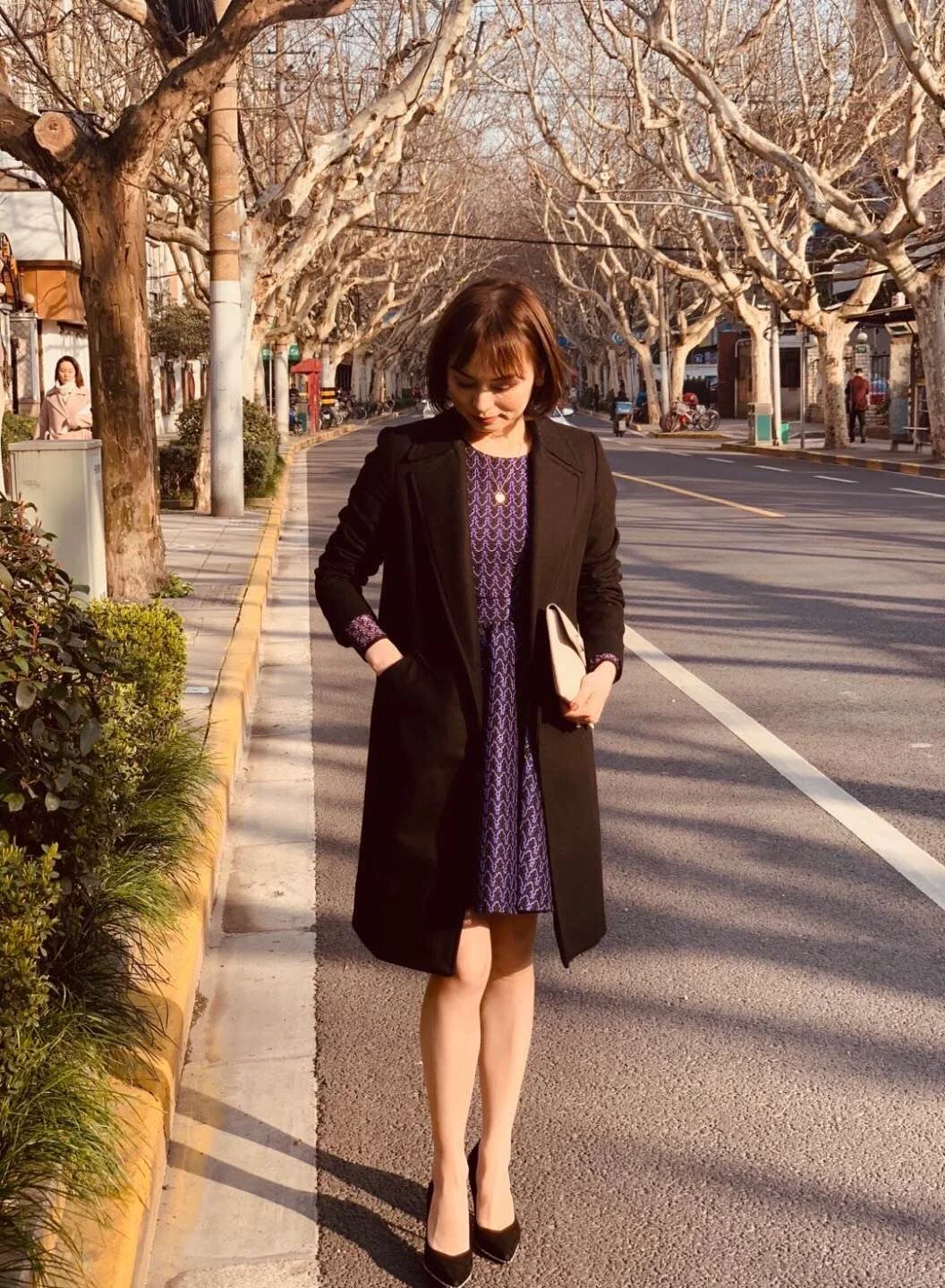Alicia walking down a tree-lined Shanghai street in a black coat