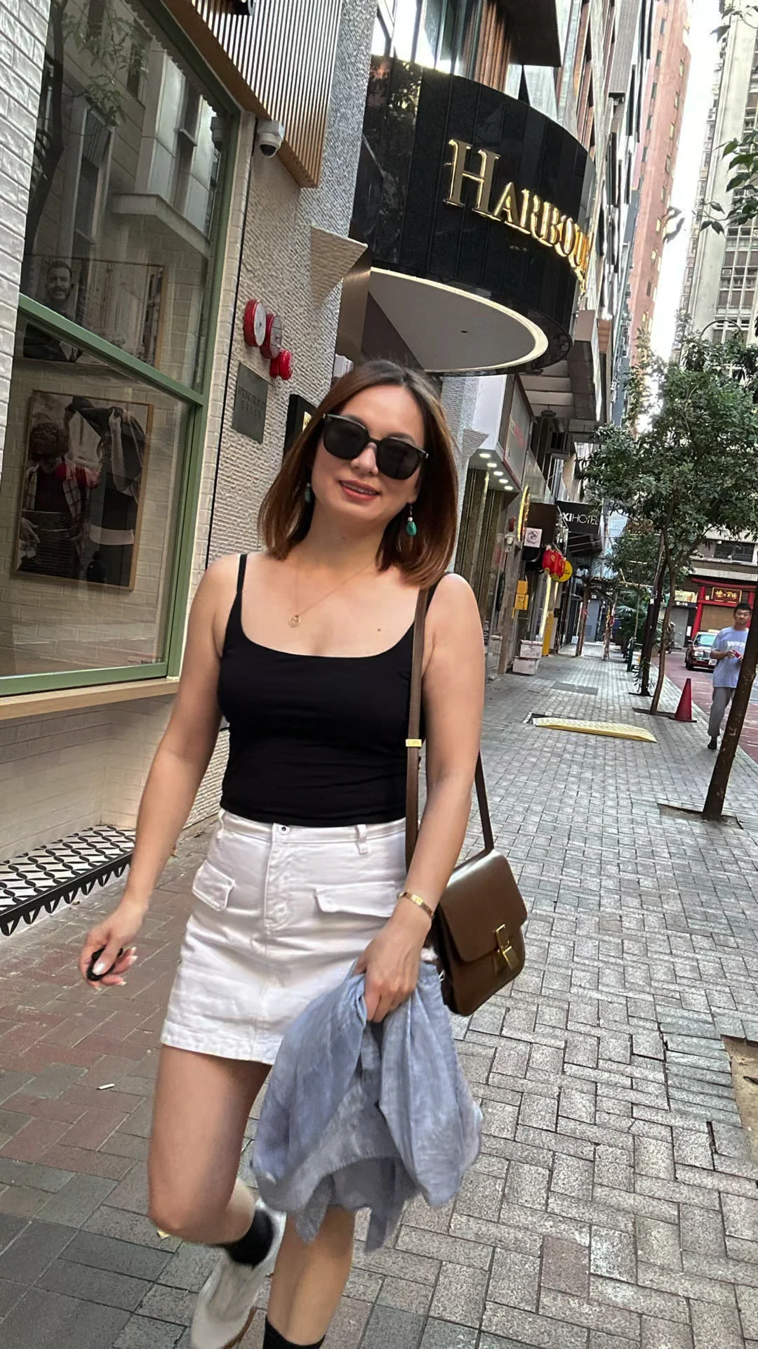 Alicia in a black camisole and white skirt on a Hong Kong street